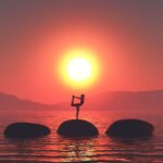 3D render of a sunset landscape with female in yoga pose on stepping stones in ocean